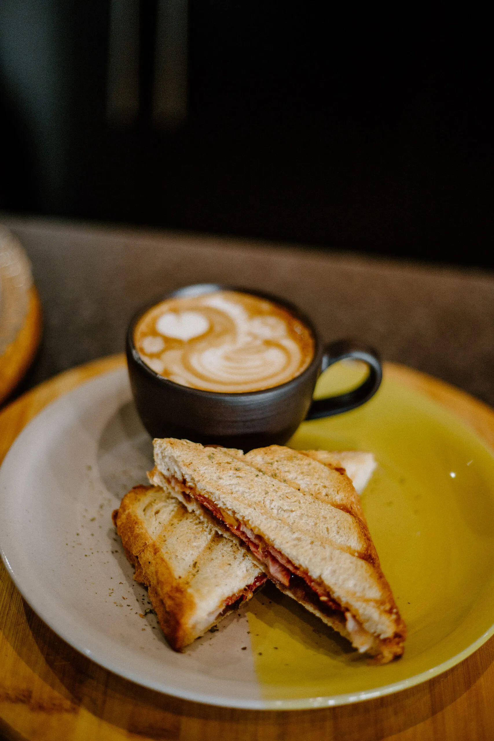 A toasted ciabatta sandwich on a yellow plate next to a flat white
