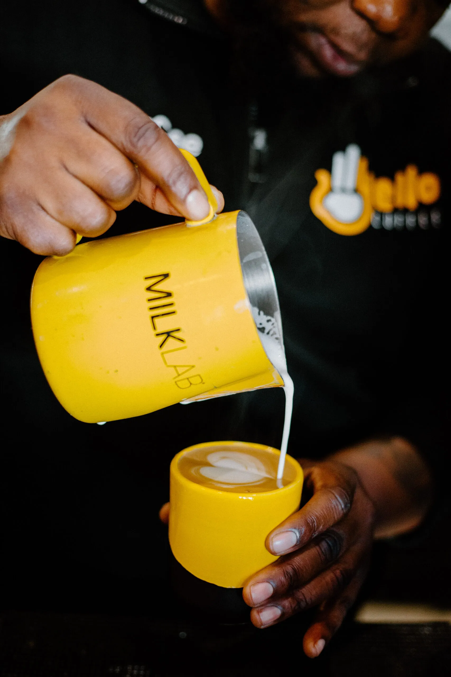 A barista pouring steamed milk from a yellow Yello Coffee jug