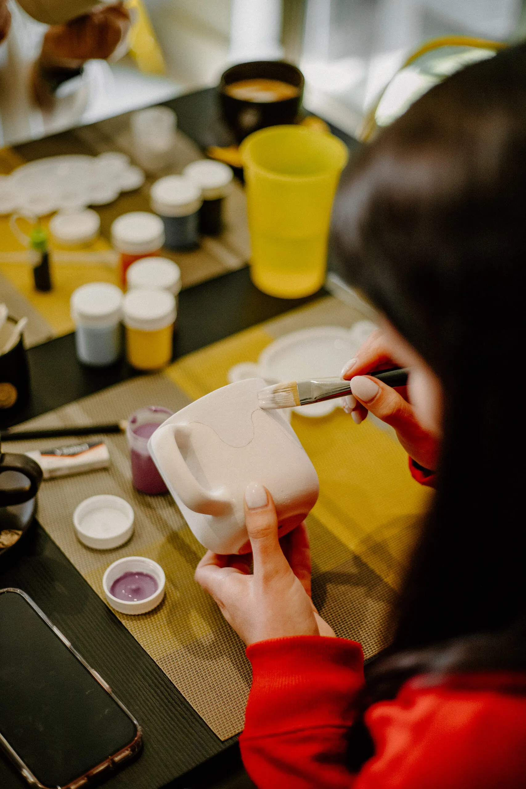 Hands painting a ceramic piece with a fine brush at a table